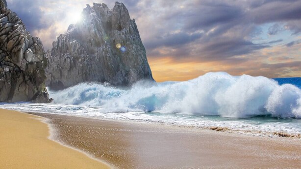 Una playa con olas rompiendo contra acantilados rocosos bajo un cielo nublado.