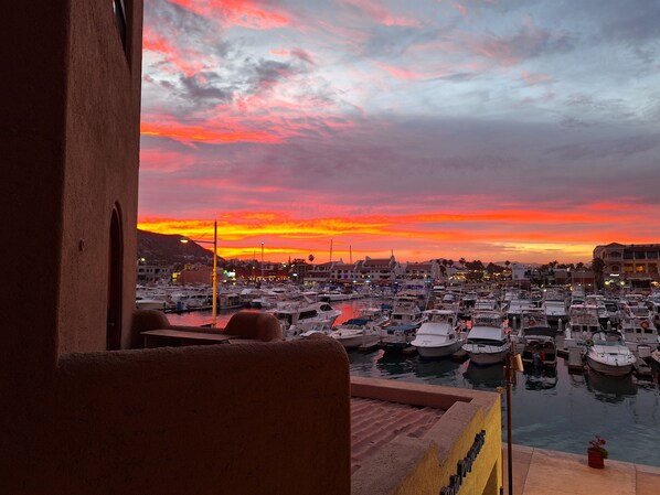 A marina with boats docked, a sunset in the background, and buildings in the distance. - Newly Renovated Cabo Marina Waterfront unit, Rooftop Pool (Cabo San Lucas)