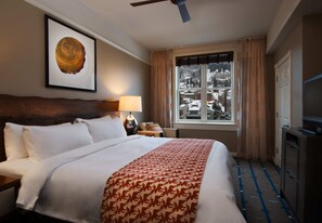 Habitación de hotel con una cama grande, un ventilador de techo, una ventana con vistas a edificios cubiertos de nieve y un televisor sobre un mueble.