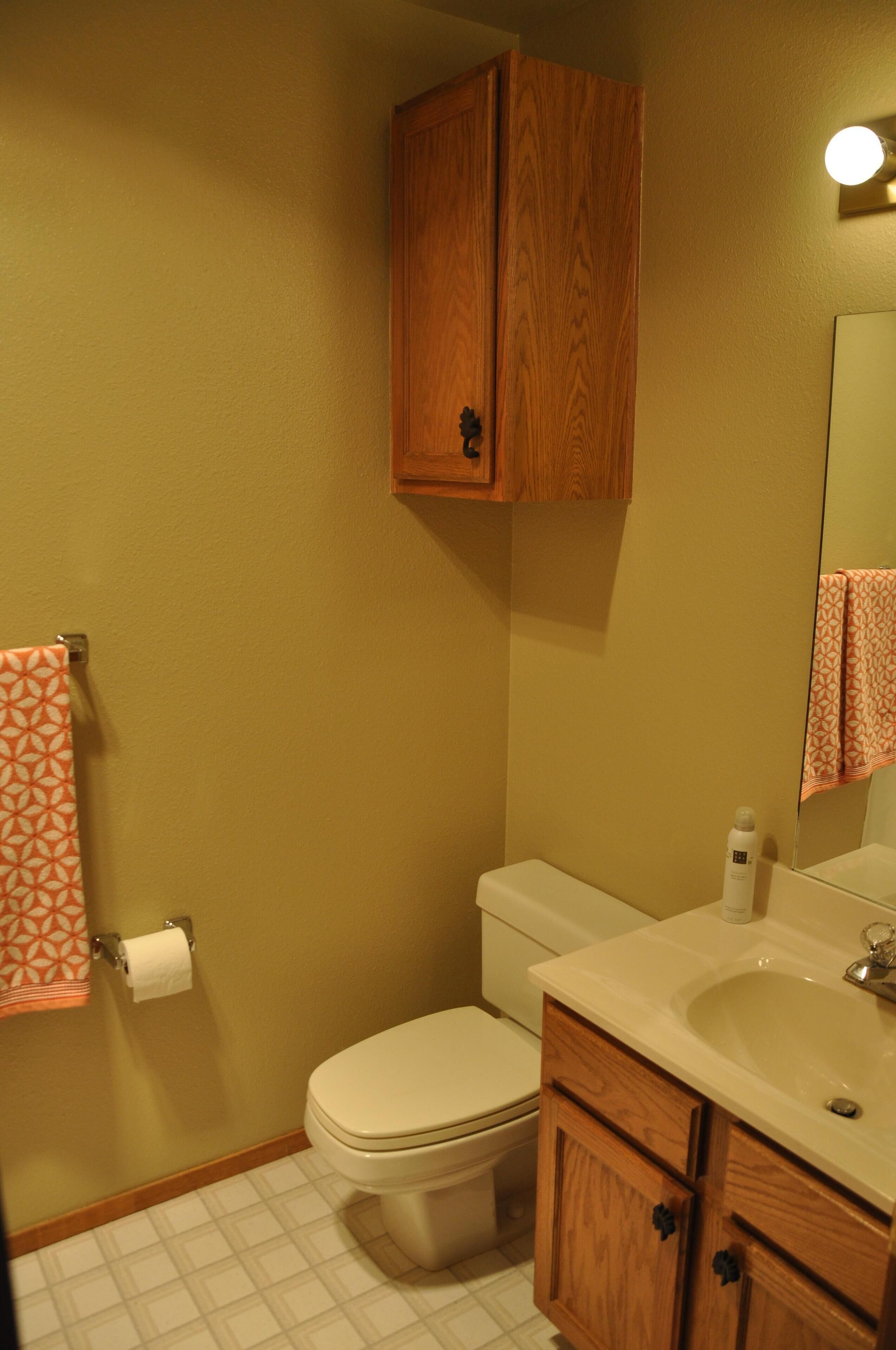 A bathroom with a toilet, sink, mirror, and wooden cabinets.