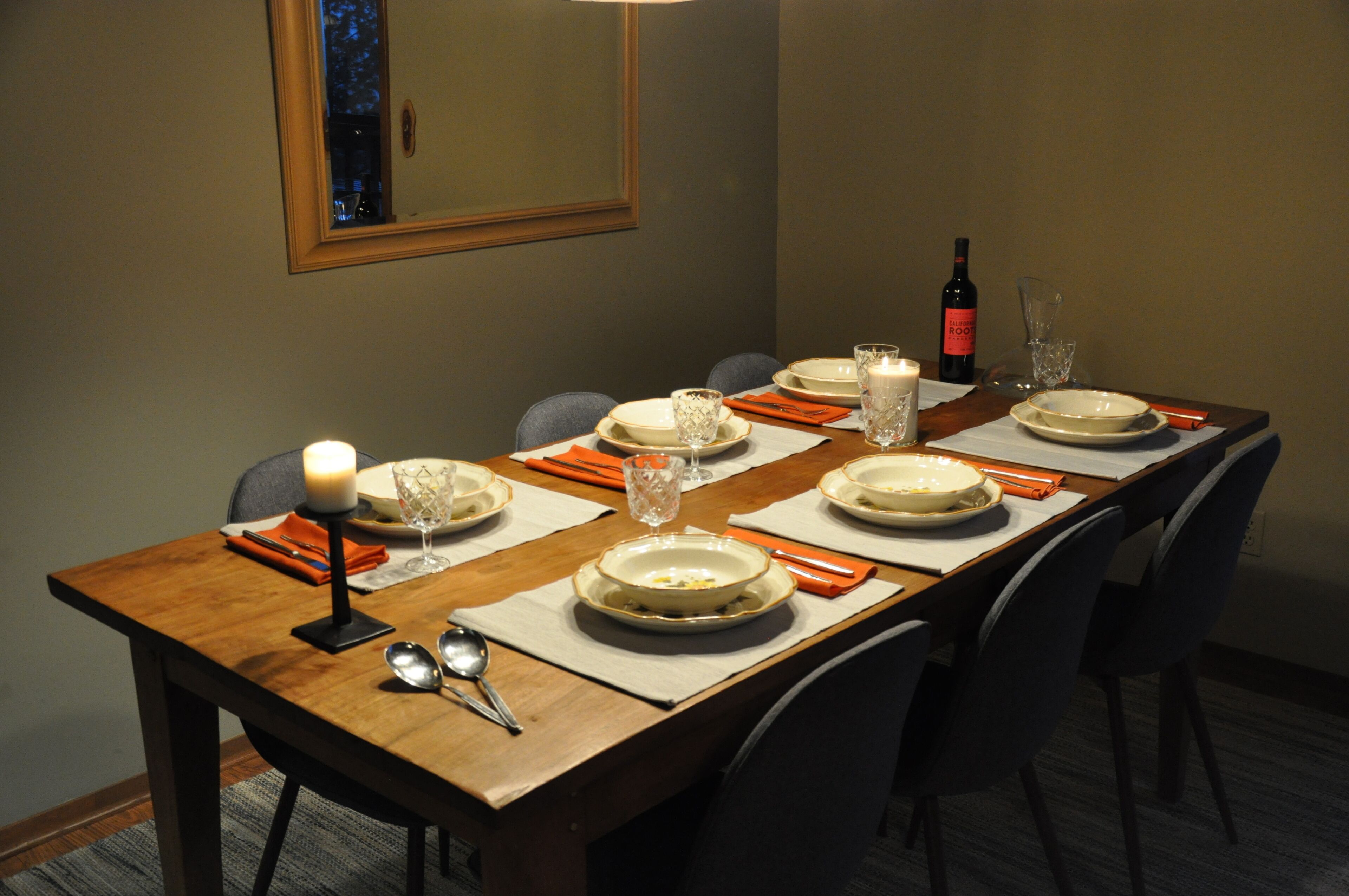 Mesa de comedor preparada para seis personas, con platos, vasos y una vela.