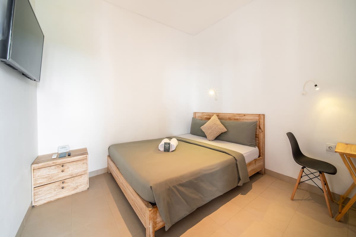 A bedroom with a bed, a wooden nightstand, a desk, and a chair.