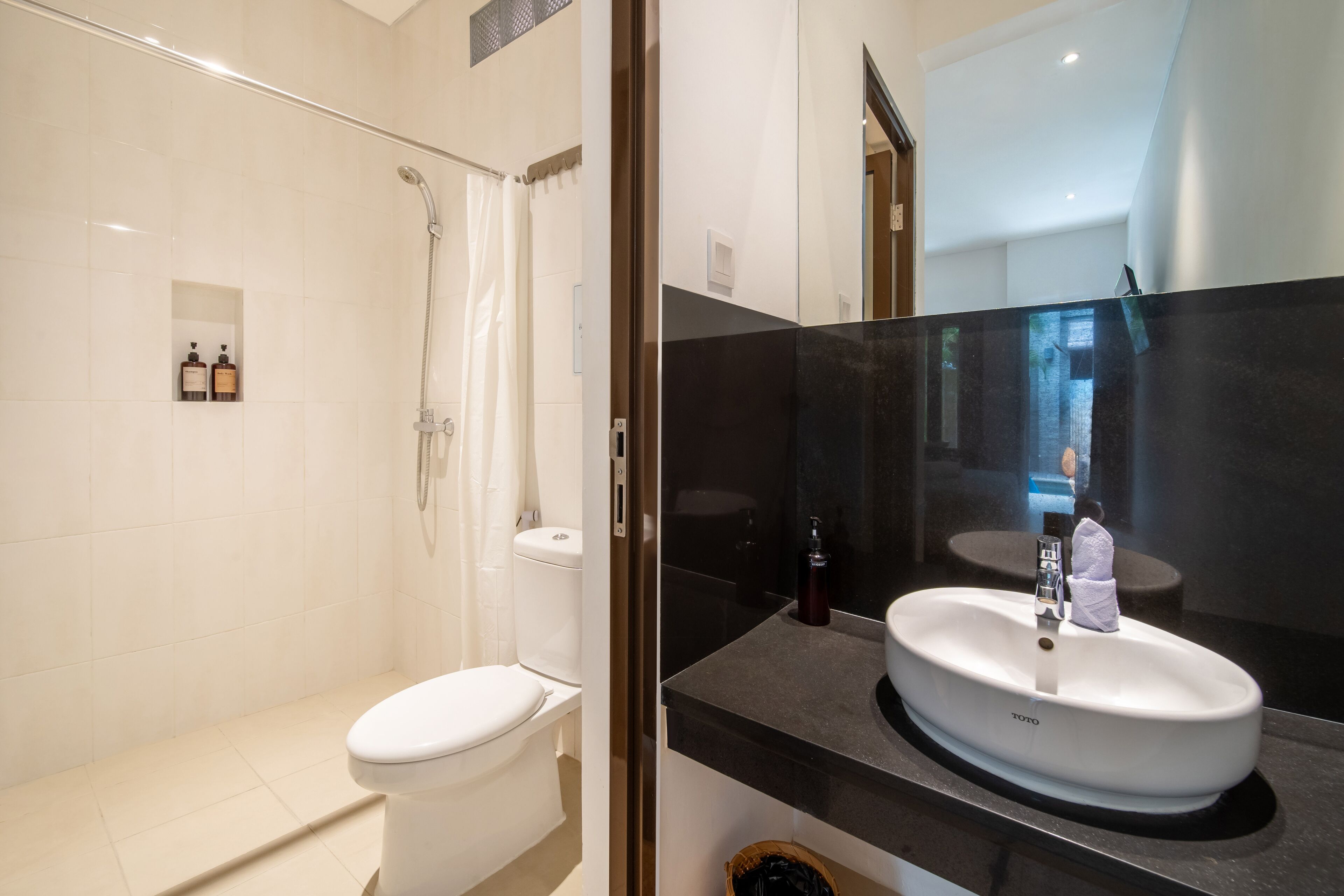 A modern bathroom with a white toilet, a glass-enclosed shower, and a black countertop with a white sink.
