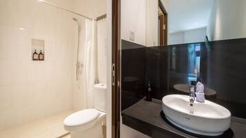 A modern bathroom with a white toilet, a glass-enclosed shower, and a black countertop with a white sink.
