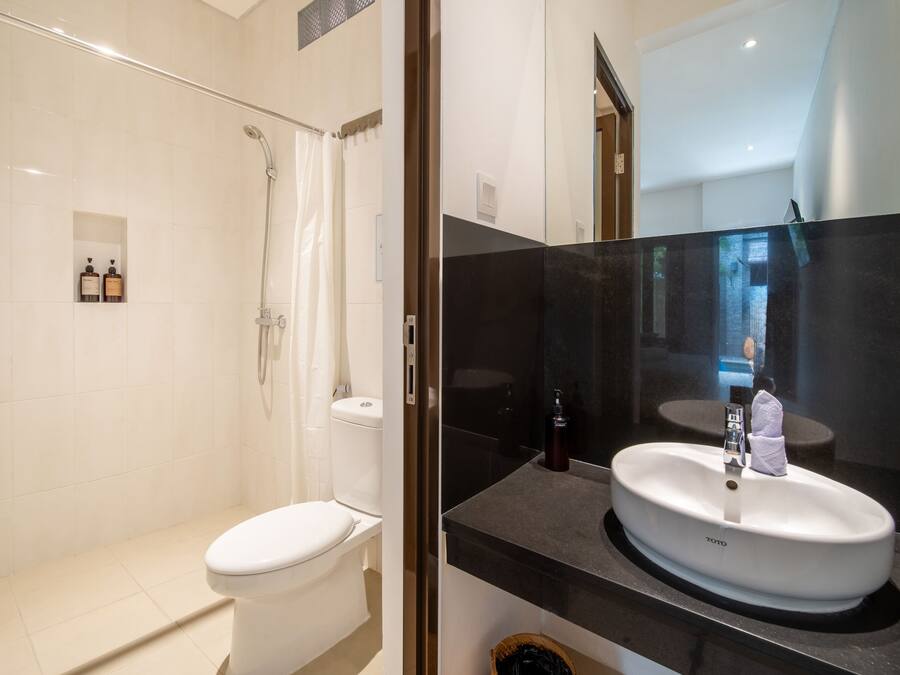 A modern bathroom with a white toilet, a glass-enclosed shower, and a black countertop with a white sink.