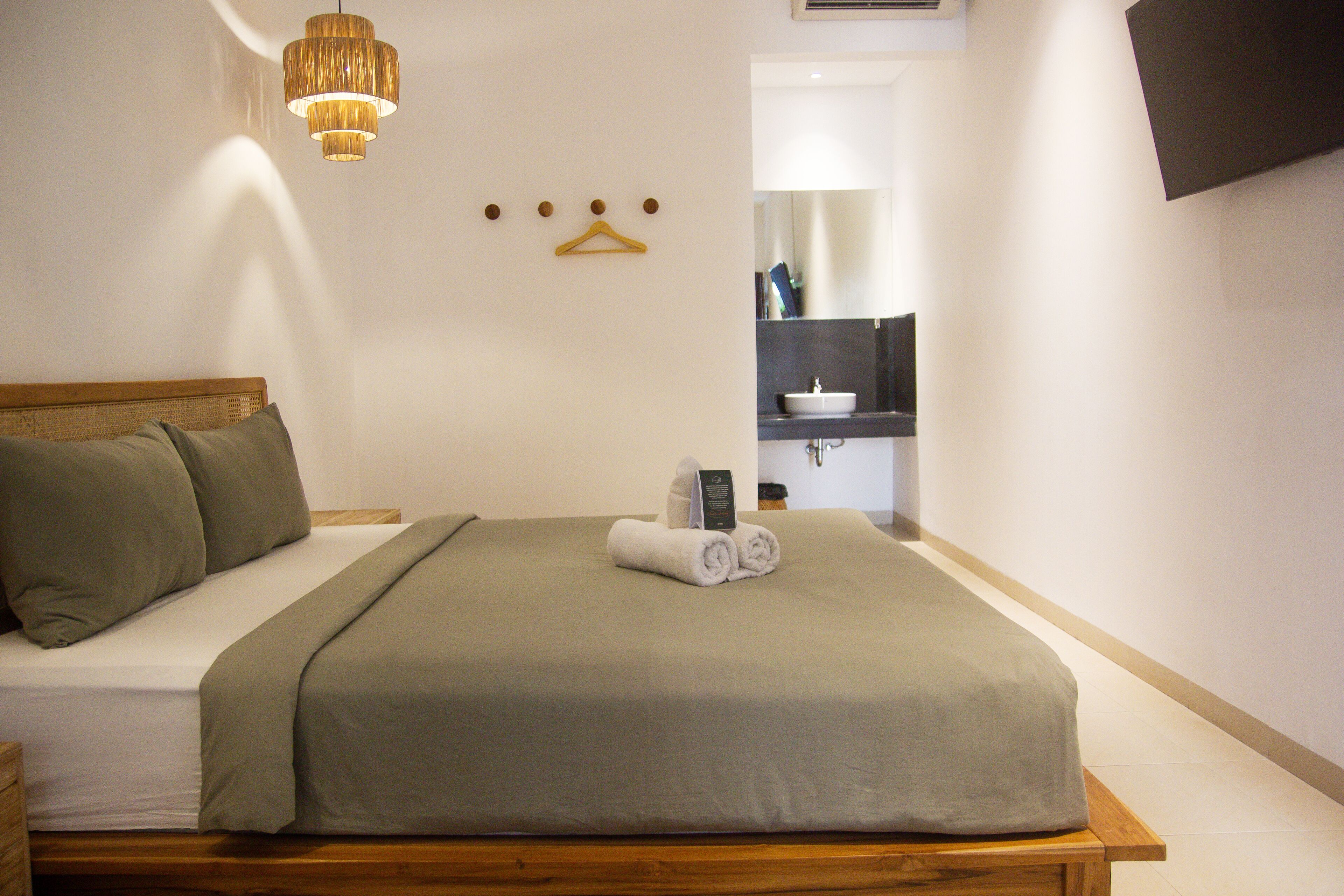 A neatly made bed with a green bedspread and pillows, a bedside table with a lamp, and a wall-mounted mirror.