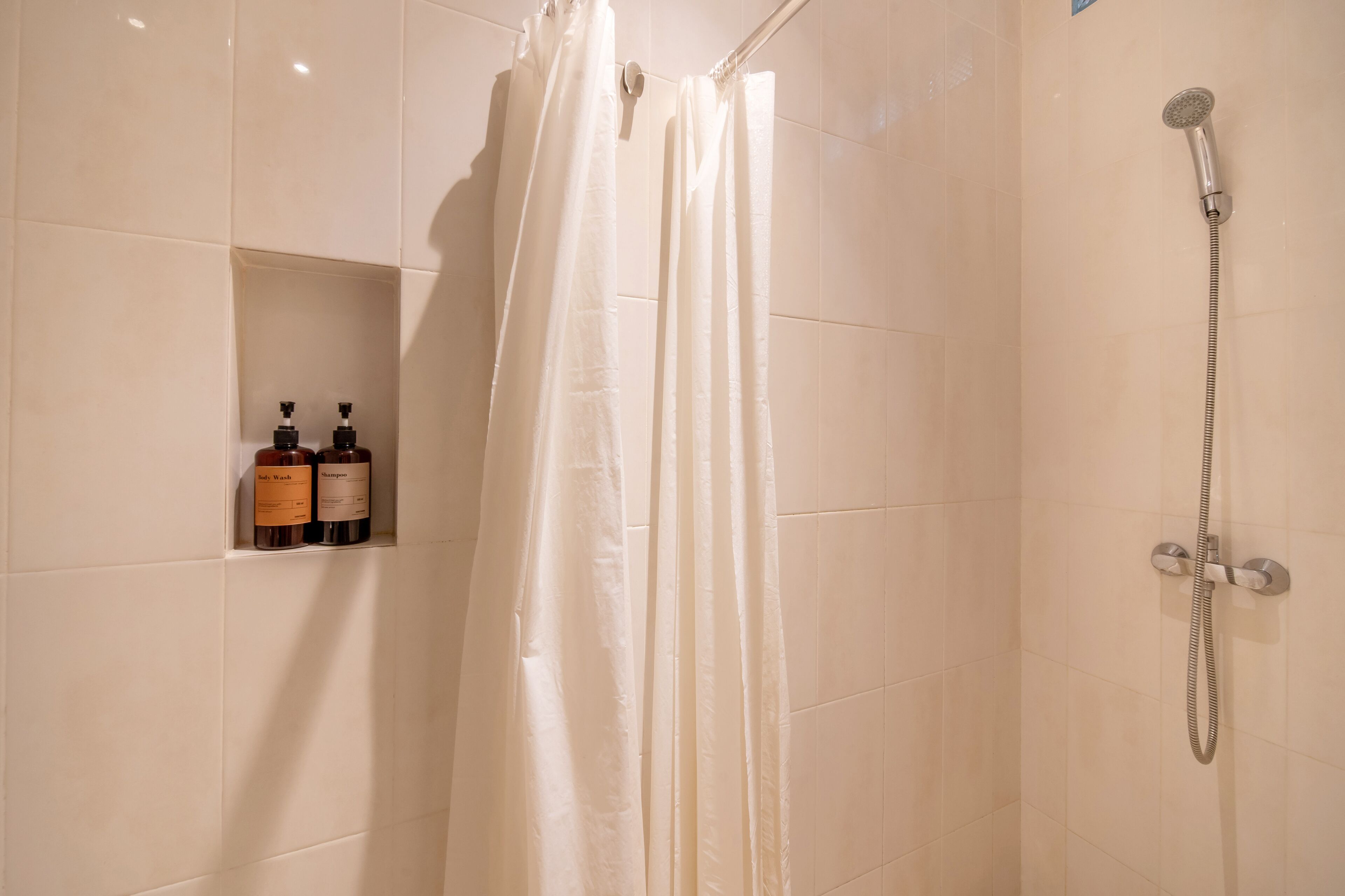 A shower area with a showerhead, a curtain, and two bottles of shampoo on a shelf.