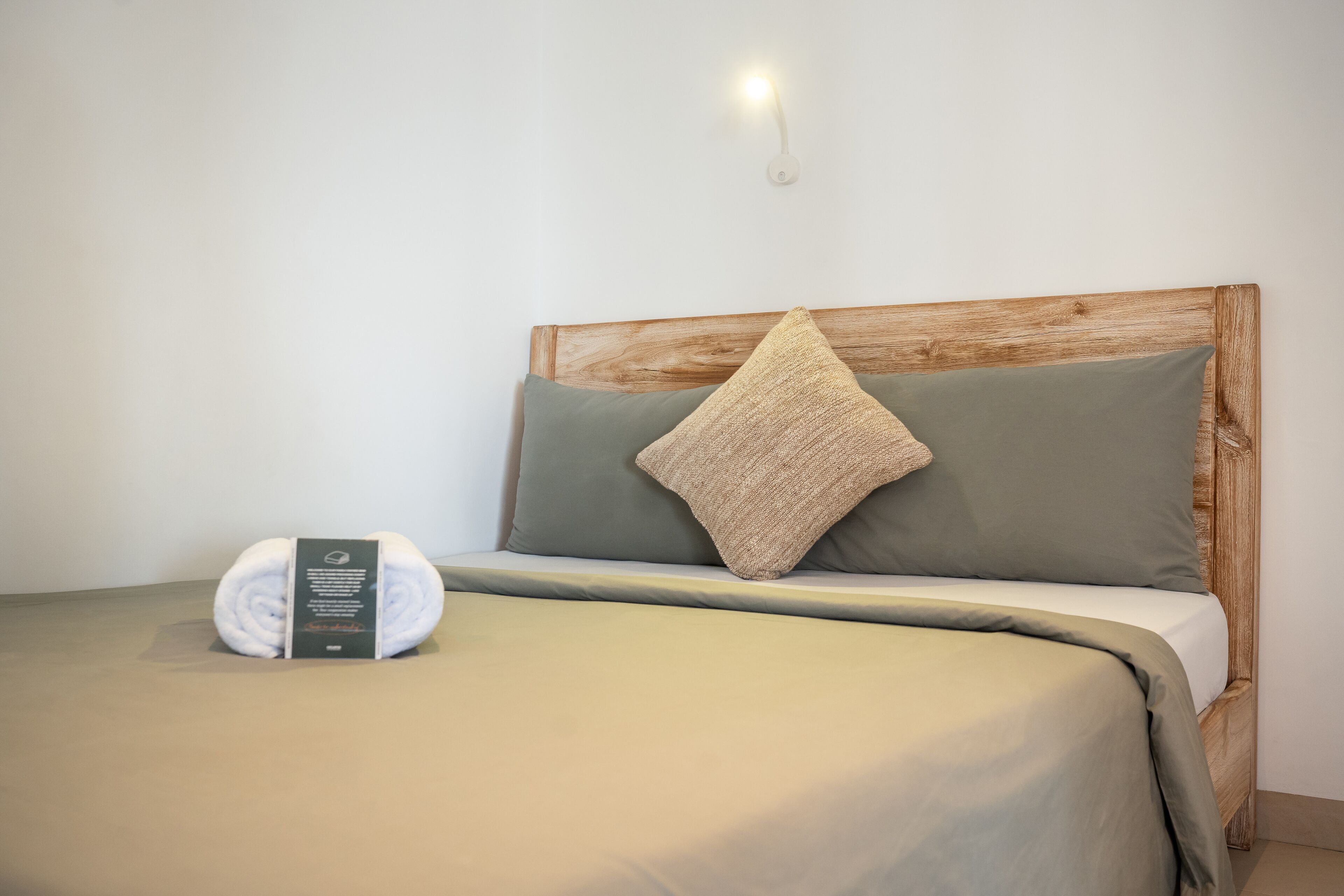 Una cama bien hecha con un cabecero de madera, una almohada verde y un edredón enrollado con una etiqueta.