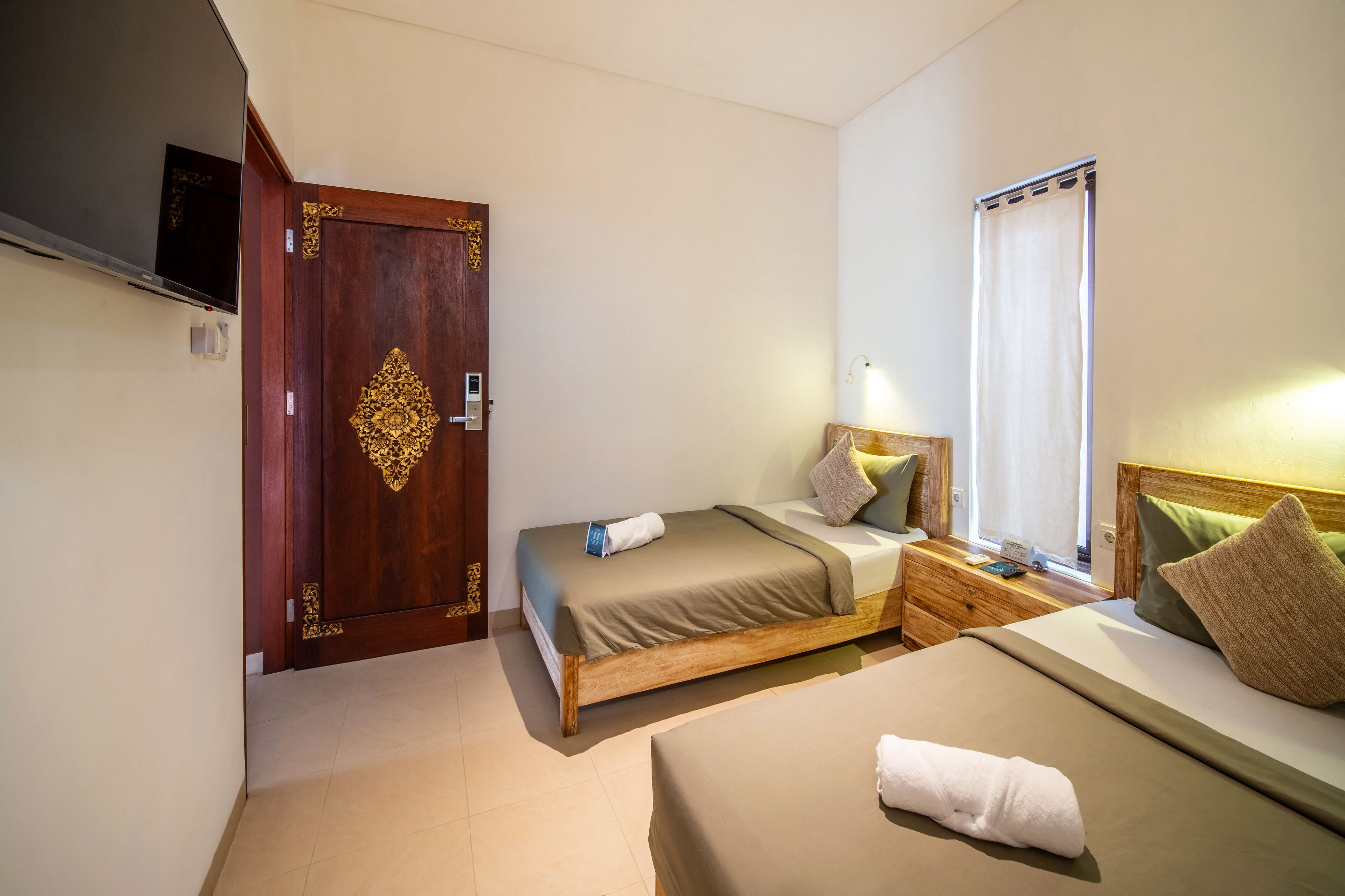 A hotel room with a wooden bed, a bedside table, a nightstand, a TV, and a window with curtains.