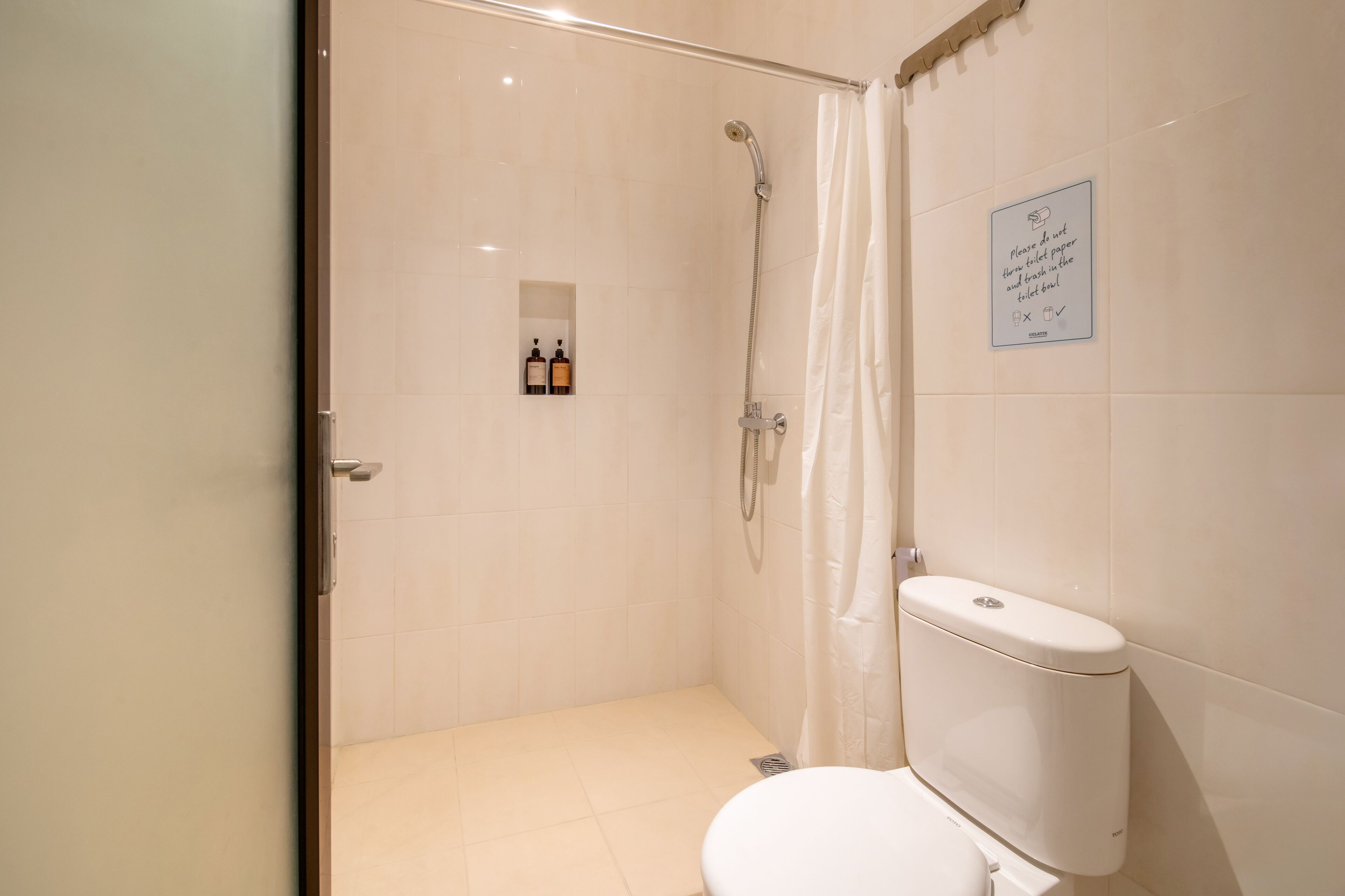 A bathroom with a shower, toilet, and a sign instructing to flush toilet paper and trash in the toilet bowl.