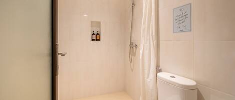 A bathroom with a shower, toilet, and a sign instructing to flush toilet paper and trash in the toilet bowl.