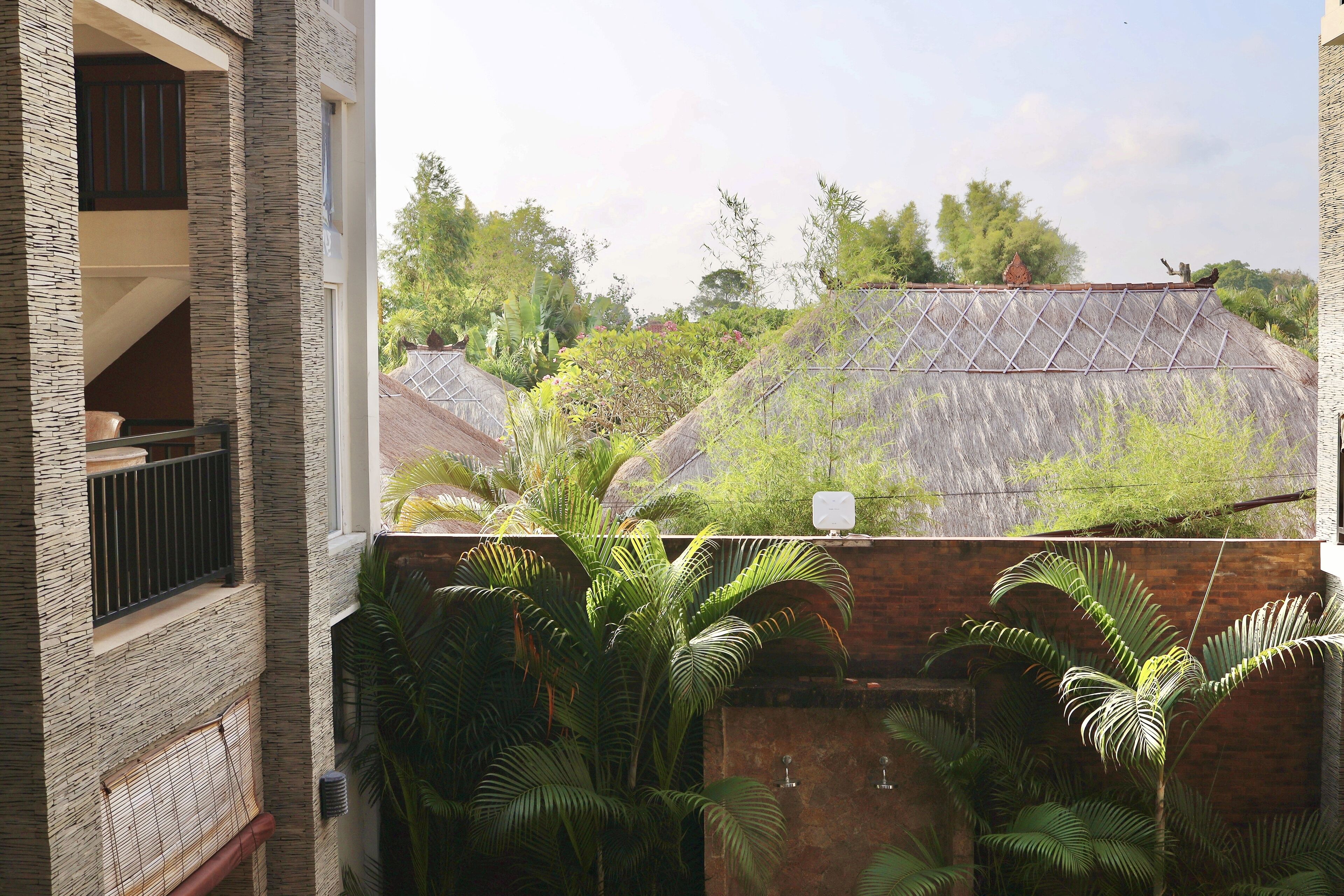 A residential area with a house featuring a balcony and a view of neighboring houses with thatched roofs.
