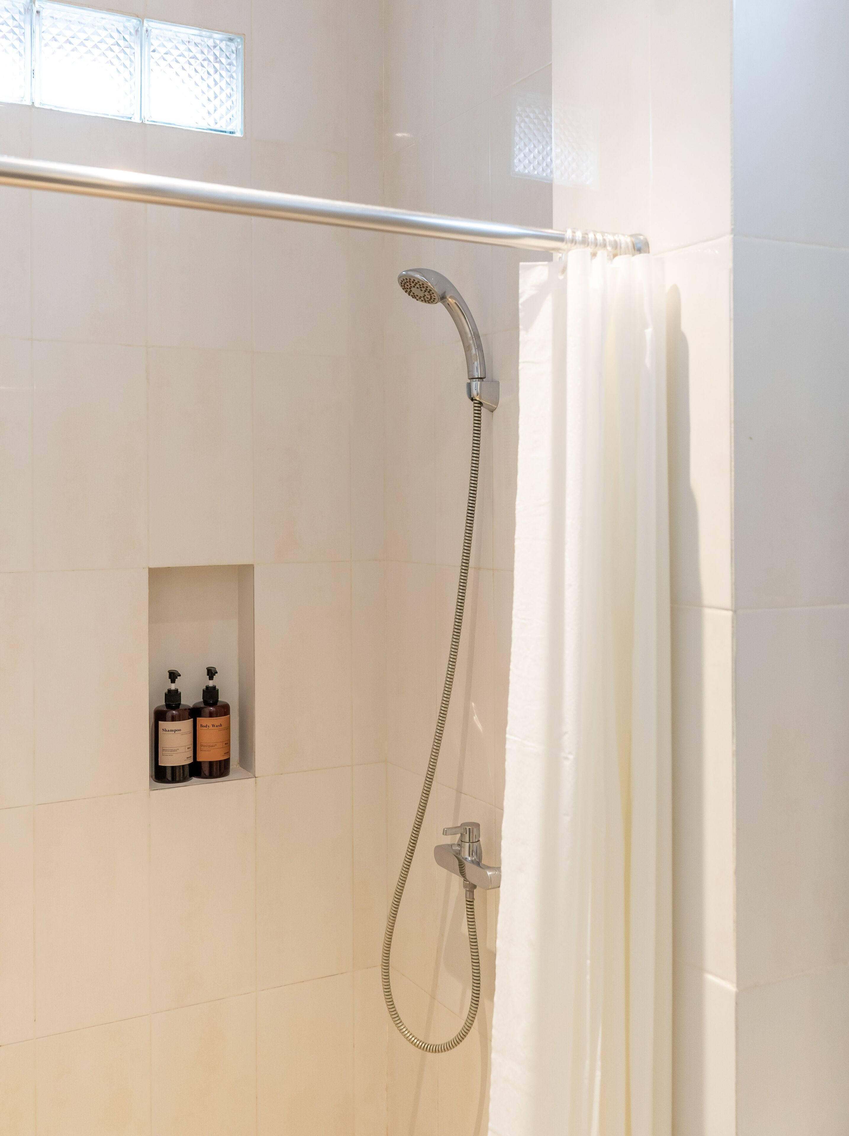 A shower area with a handheld showerhead, a curtain, and two bottles of shampoo and body wash.
