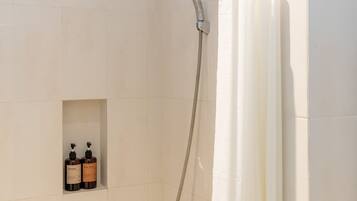 A shower area with a handheld showerhead, a curtain, and two bottles of shampoo and body wash.