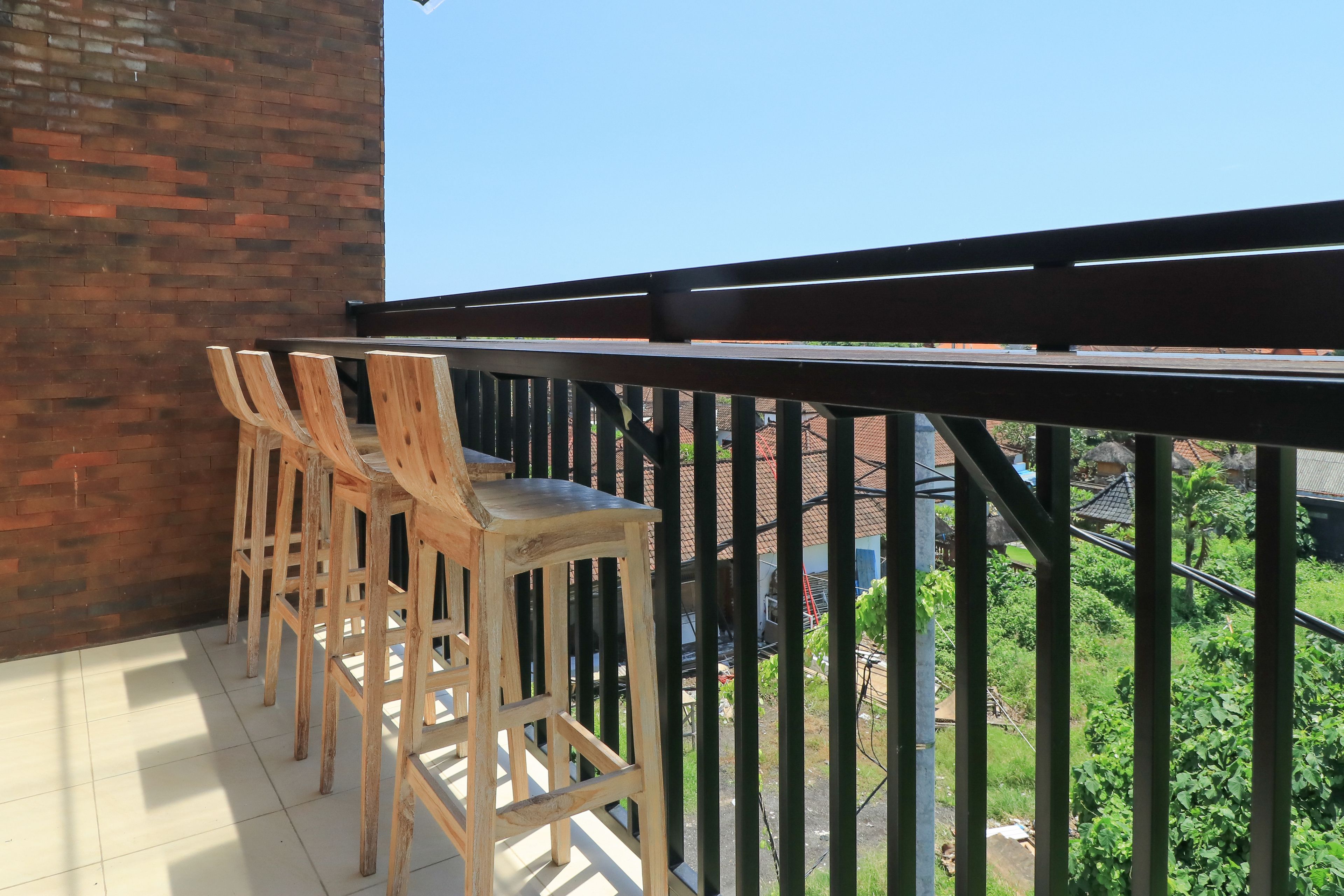 A balcony with wooden chairs and a view of a green landscape and buildings.