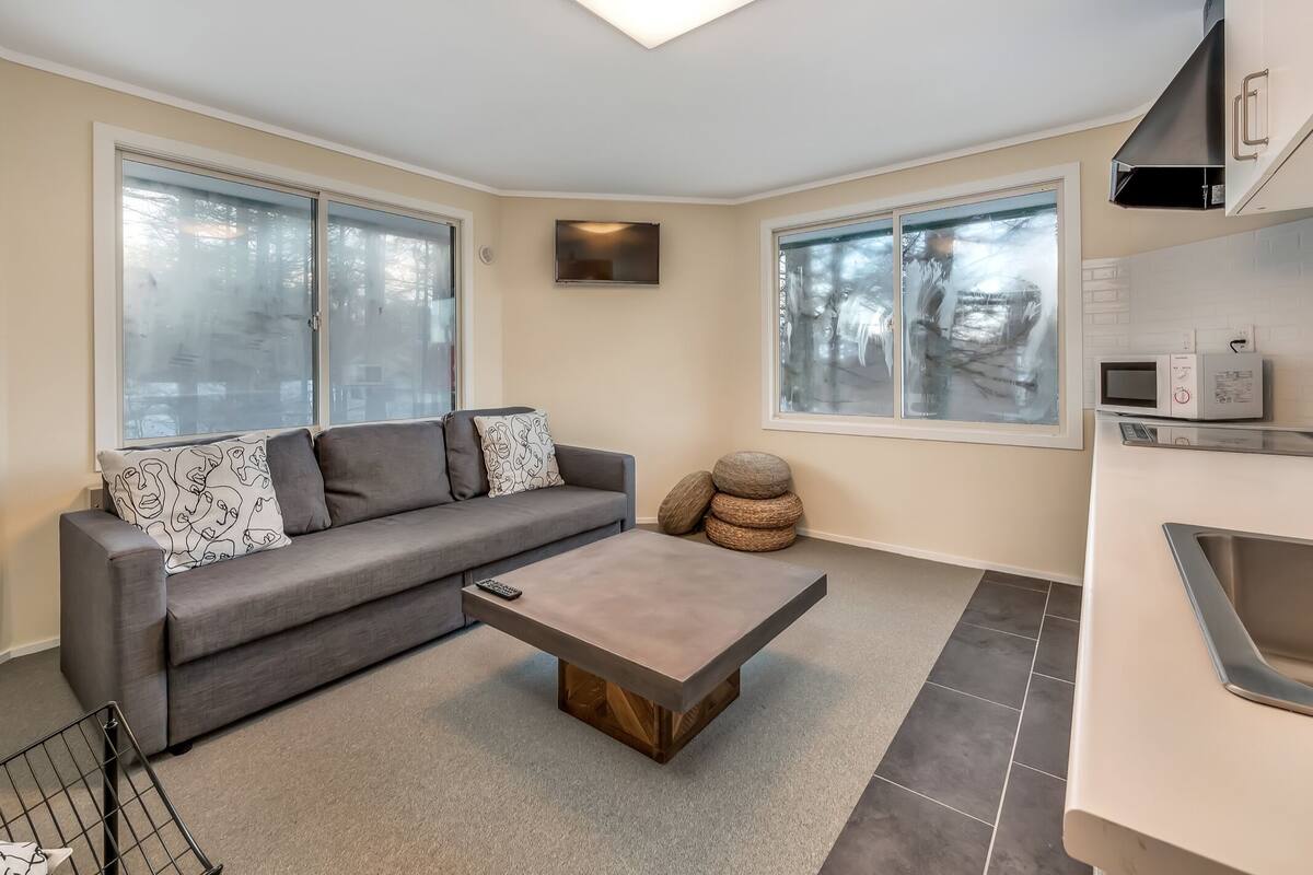 A modern living room with a grey sofa, a coffee table, and a kitchen area with a microwave.