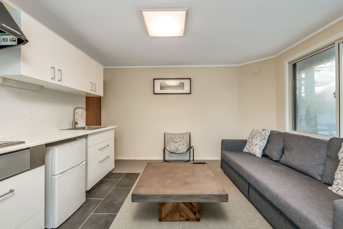 A modern kitchen with white cabinets, a built-in oven, and a grey sofa with patterned cushions.