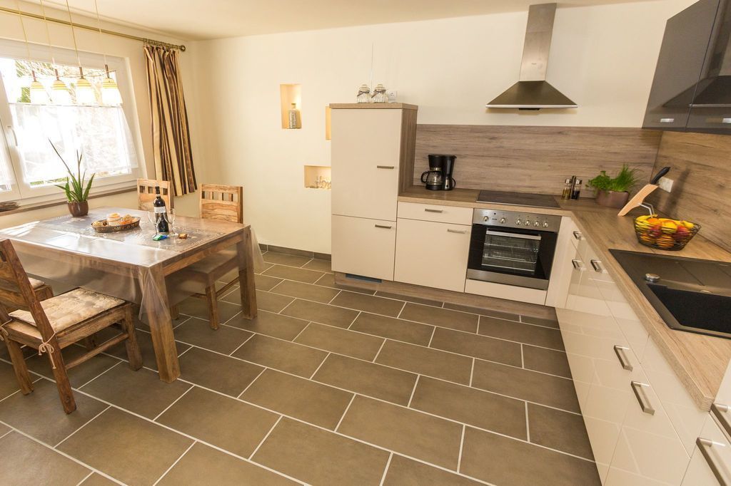 A modern kitchen with a dining table, chairs, a refrigerator, oven, and a sink.