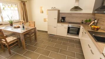 A modern kitchen with a dining table, chairs, a refrigerator, oven, and a sink.
