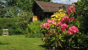 A rustic wooden house with a sloped roof, surrounded by lush greenery and vibrant flowers. - Wildnisresidenz am Nationalpark (Lindberg)