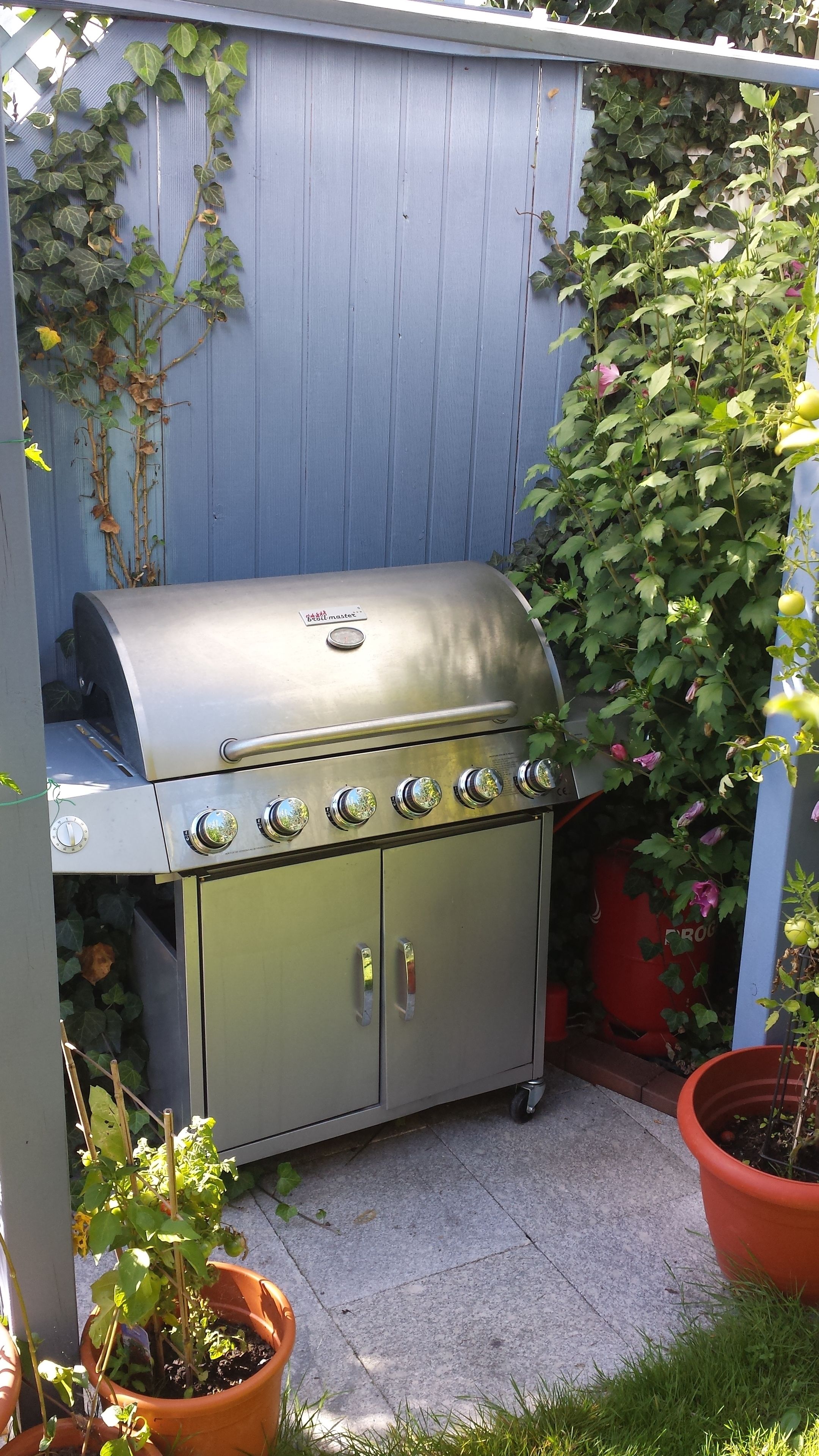 Ein Edelstahlgrill mit vier Brennern, einer seitlichen Tür und einem Schornstein.