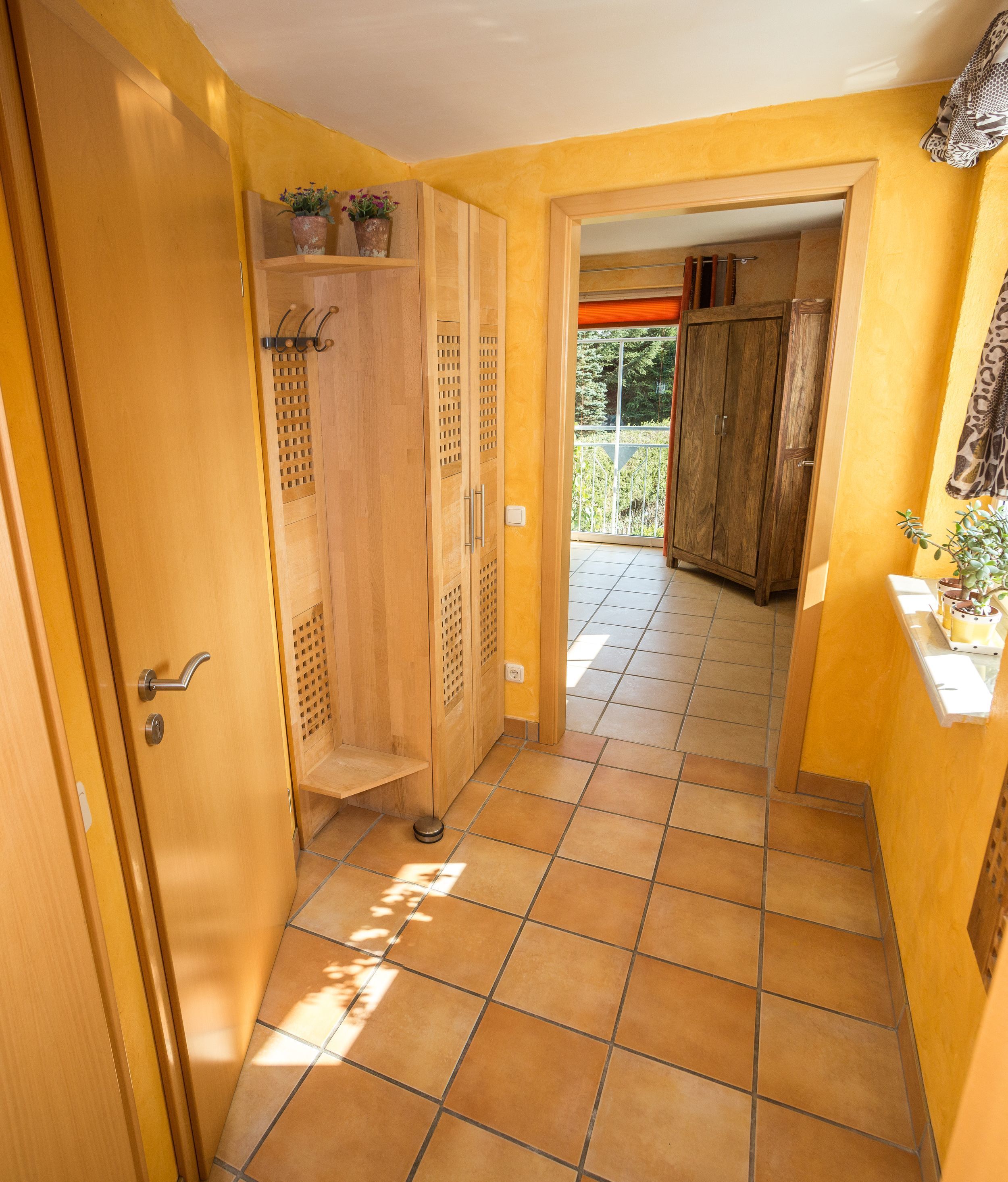 Un pasillo con puertas de madera, piso de baldosas y vistas a un balcón con barandilla.