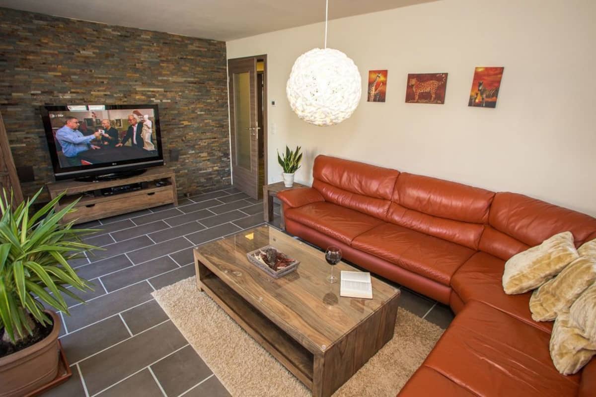Una sala de estar moderna con un sofá de cuero, una mesa de centro de madera, un televisor sobre un mueble de madera y una pared de piedra.