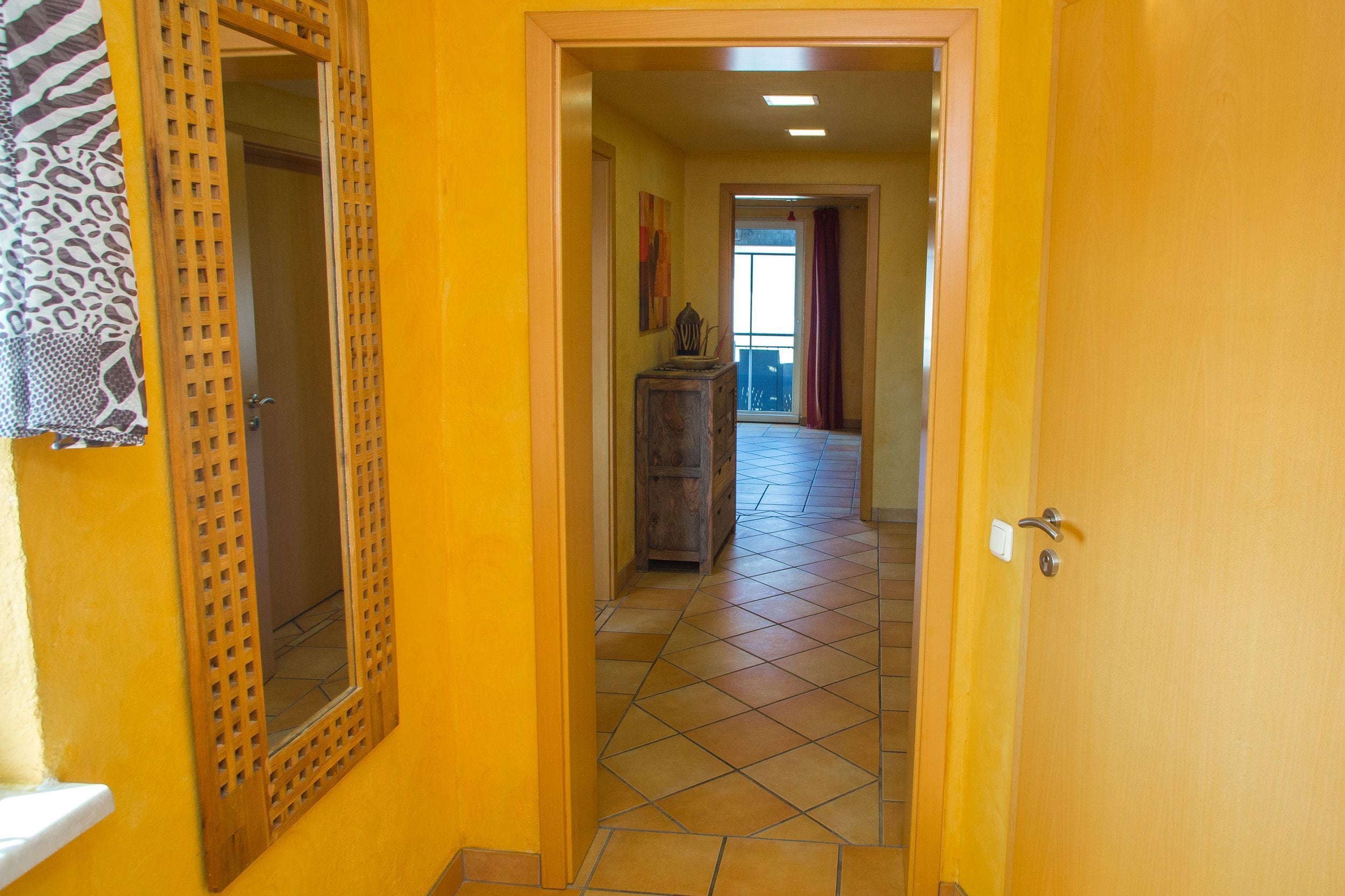A hallway with a wooden door, a mirror, and a tiled floor.