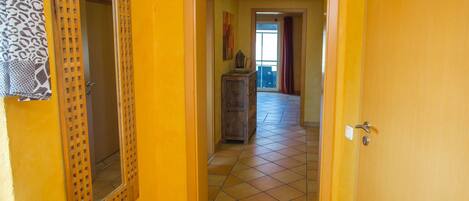 A hallway with a wooden door, a mirror, and a tiled floor.