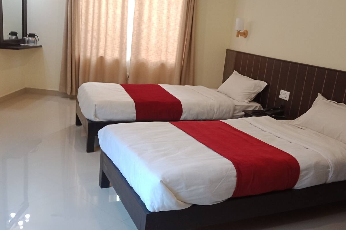 A hotel room with two beds, a mirror, a nightstand, and a window with curtains.