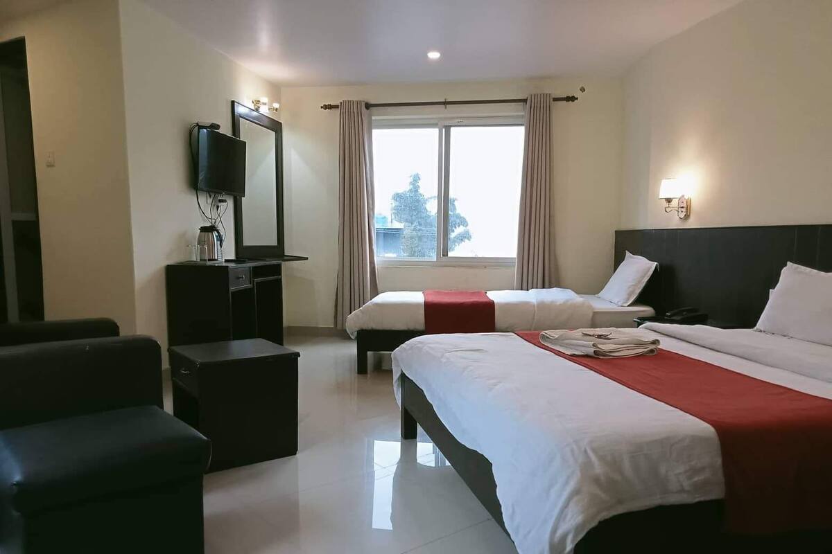 A hotel room with two beds, a TV, a desk, and a window with curtains.