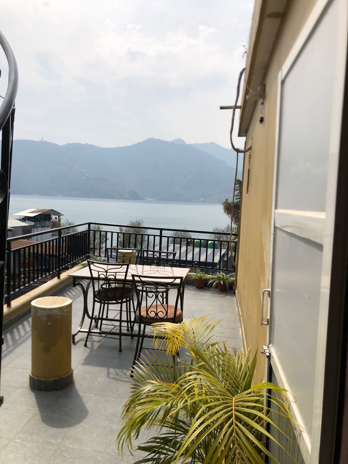 A balcony with a table and chairs, overlooking a lake and mountains.