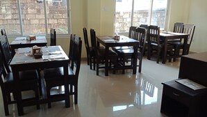 A dining area with wooden tables and chairs, a tiled floor, and a view of a brick wall through the windows. - Hotel My Dream (Pokhara)