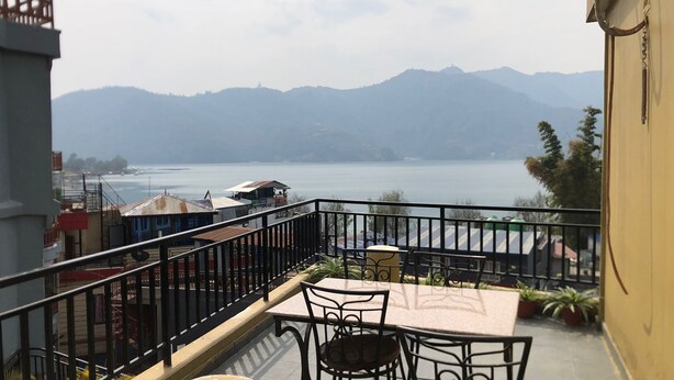 A balcony with a table and chairs, overlooking a body of water and mountains. - Hotel My Dream (Pokhara)