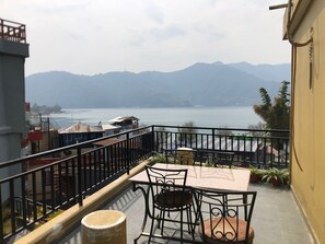 A balcony with a table and chairs, overlooking a body of water and mountains. - Hotel My Dream (Pokhara)