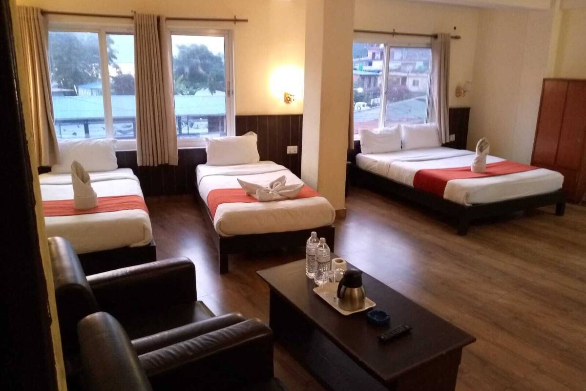A hotel room with three beds, a sofa, a coffee table, and a view of the outside.