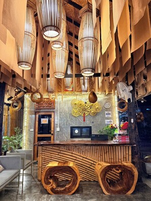 Un área de recepción con un mostrador de madera, decoración de pared de bambú y lámparas colgantes de bambú.