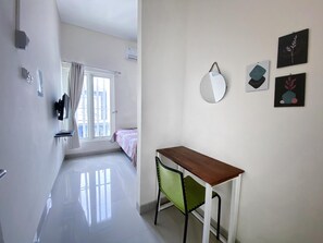 A modern, well-lit room with a wooden desk, a green chair, and a large window with curtains.