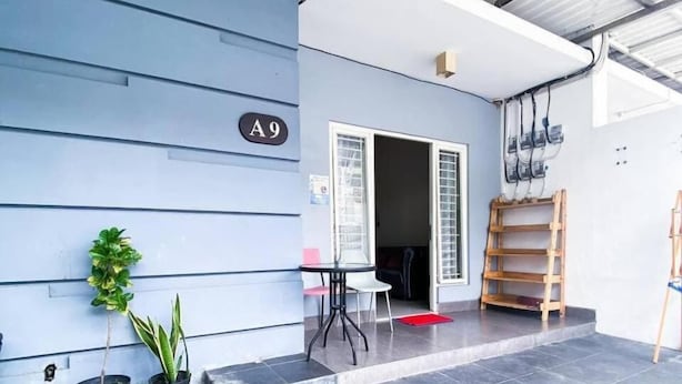 Een modern gebouw met een blauwe gevel, een betegeld terras, en een kleine tuin met potplanten.