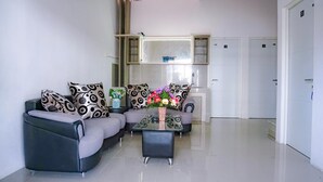 Een moderne woonkamer met een grijze zithoek, een bijzettafel met bloemen en een keukenhoek met kastjes en een magnetron.