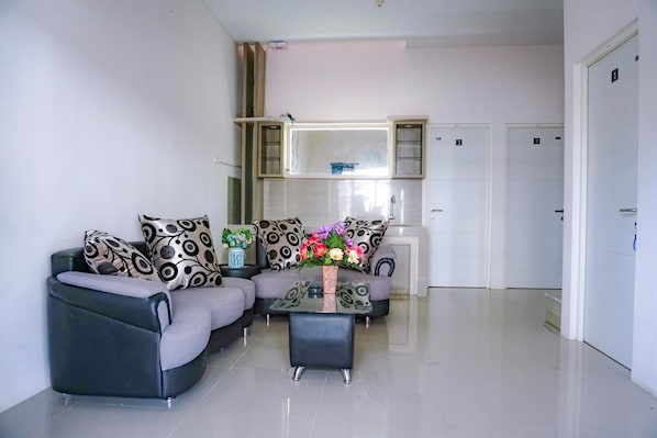 A modern living room with a grey sofa set, a coffee table with flowers, and a kitchen area with cabinets and a microwave.