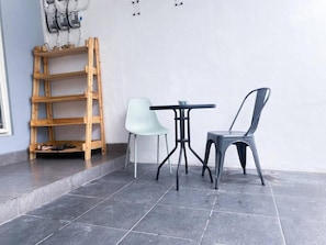 Une petite pièce carrelée, avec une échelle en bois, une chaise blanche, une table noire et une chaise grise.
