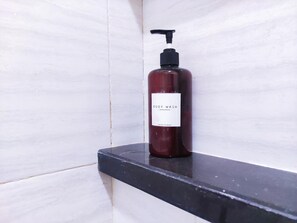Une bouteille de gel douche sur un comptoir noir, devant un mur recouvert de carreaux blancs.