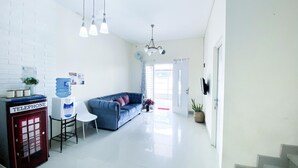 Een moderne woonkamer met een blauwe bank, een witte salontafel, een rode telefooncel en een waterdispenser.