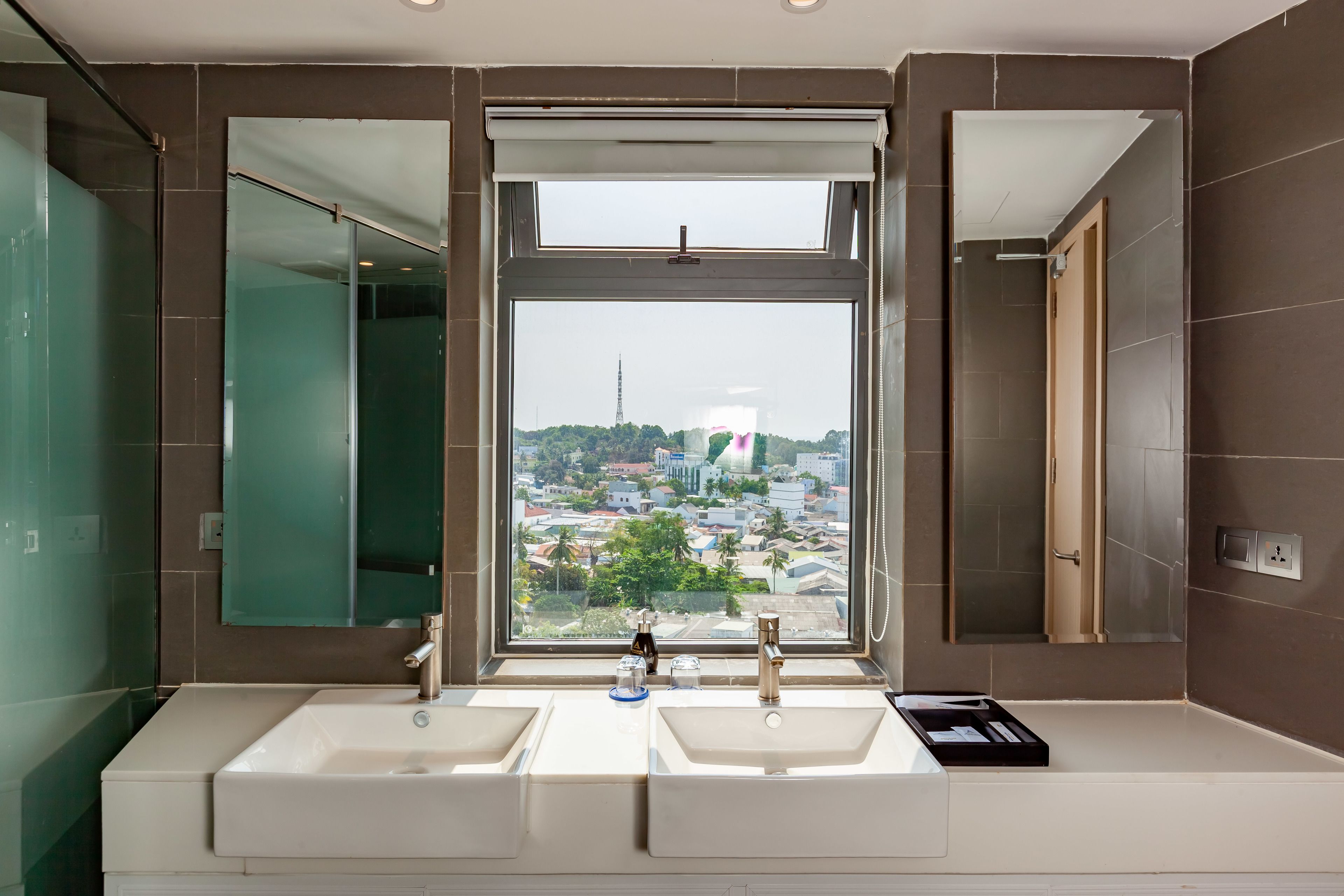 Een badkamer met twee wasbakken, een grote spiegel en een raam met uitzicht over de stad.