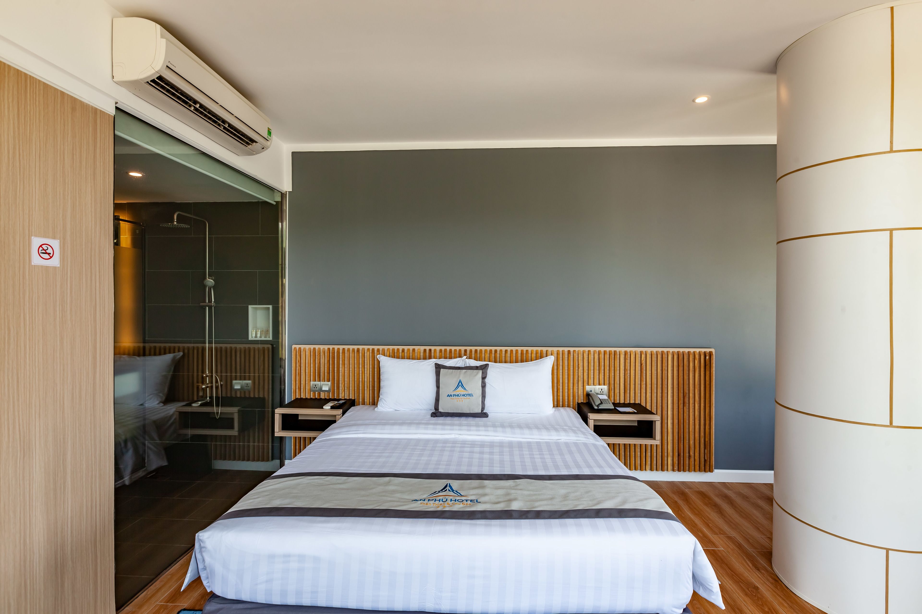 Een hotelkamer met een bed, nachtkastjes, een douche en een wandmodel airconditioner.