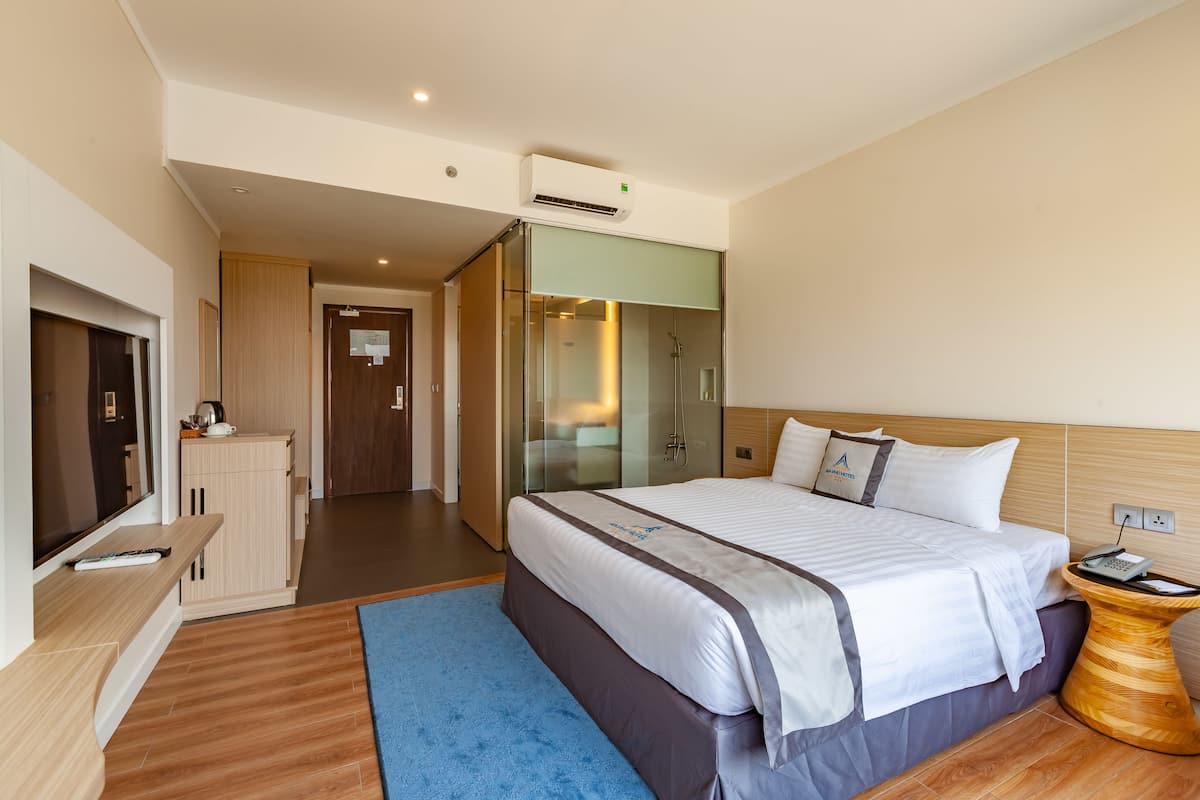 Habitación de hotel con una cama grande, un televisor, un escritorio y un baño con ducha de vidrio.