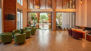 A modern hotel lobby with a reception desk, green and red seating, and large windows offering views of the street. - An Phu Hotel (Phu Quoc)
