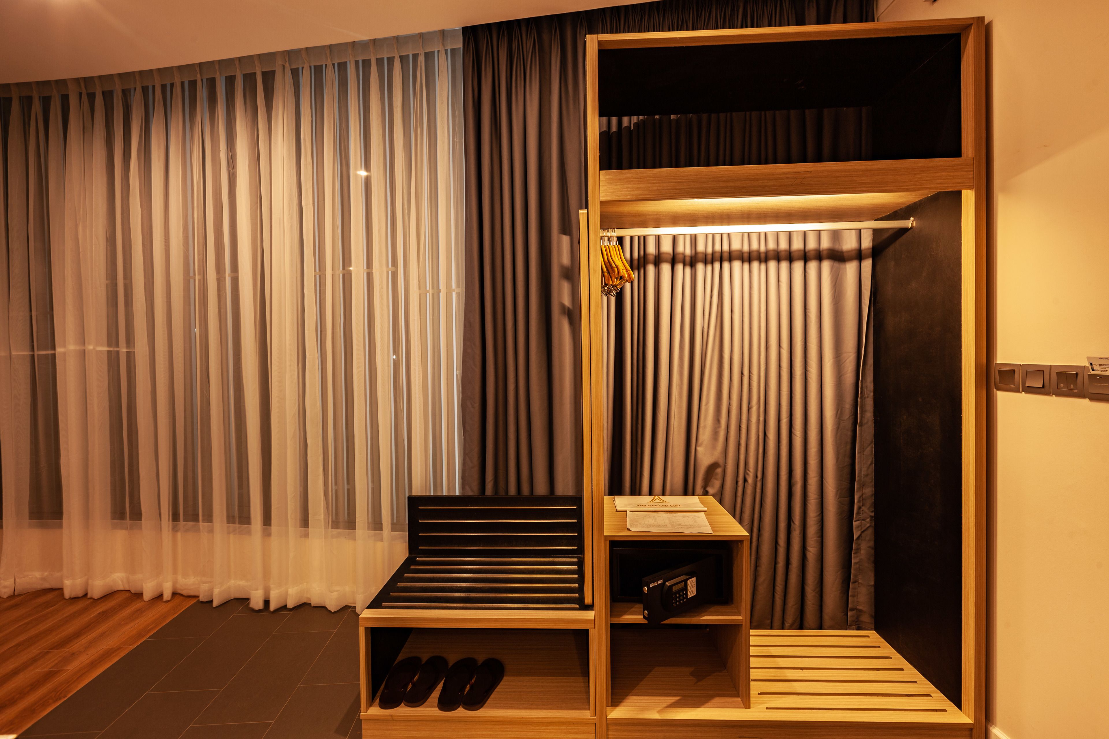 A room with a bed, a wooden shelf with shoes, a small table with a lamp, and a curtain.