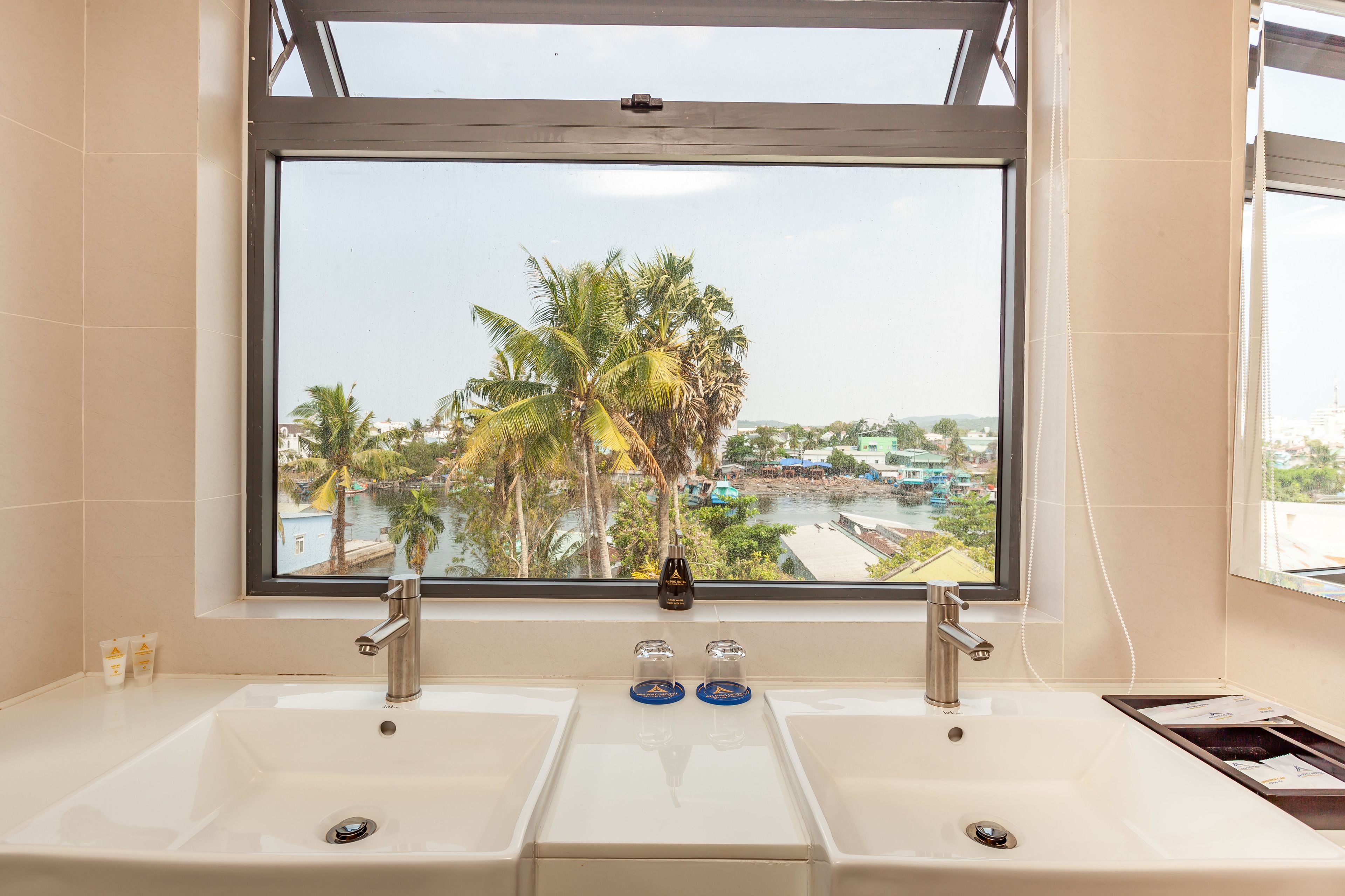 A bathroom with a large window, two sinks, and a view of palm trees and a river.